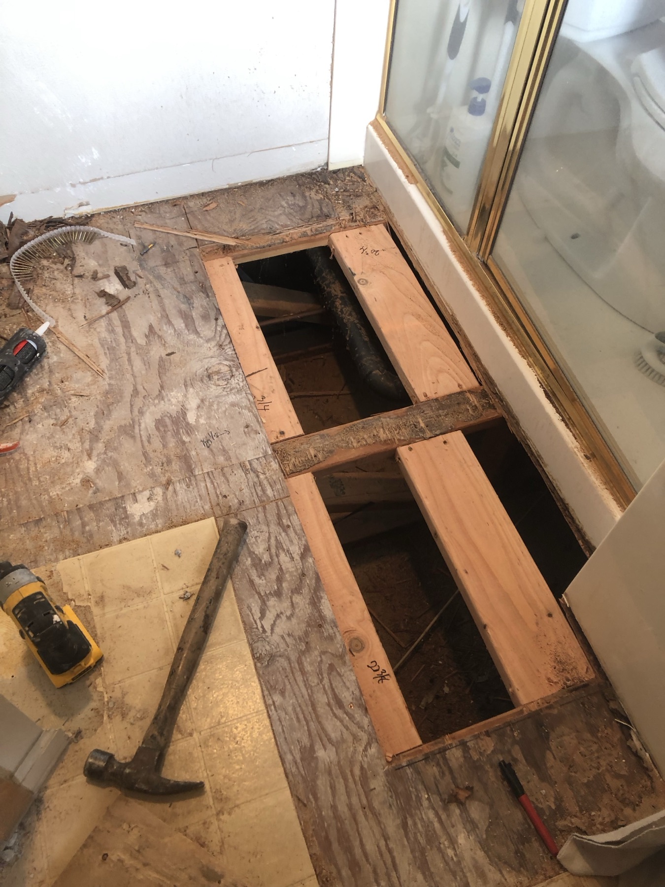 Bathroom floor opened down to the joists beside a glass shower door