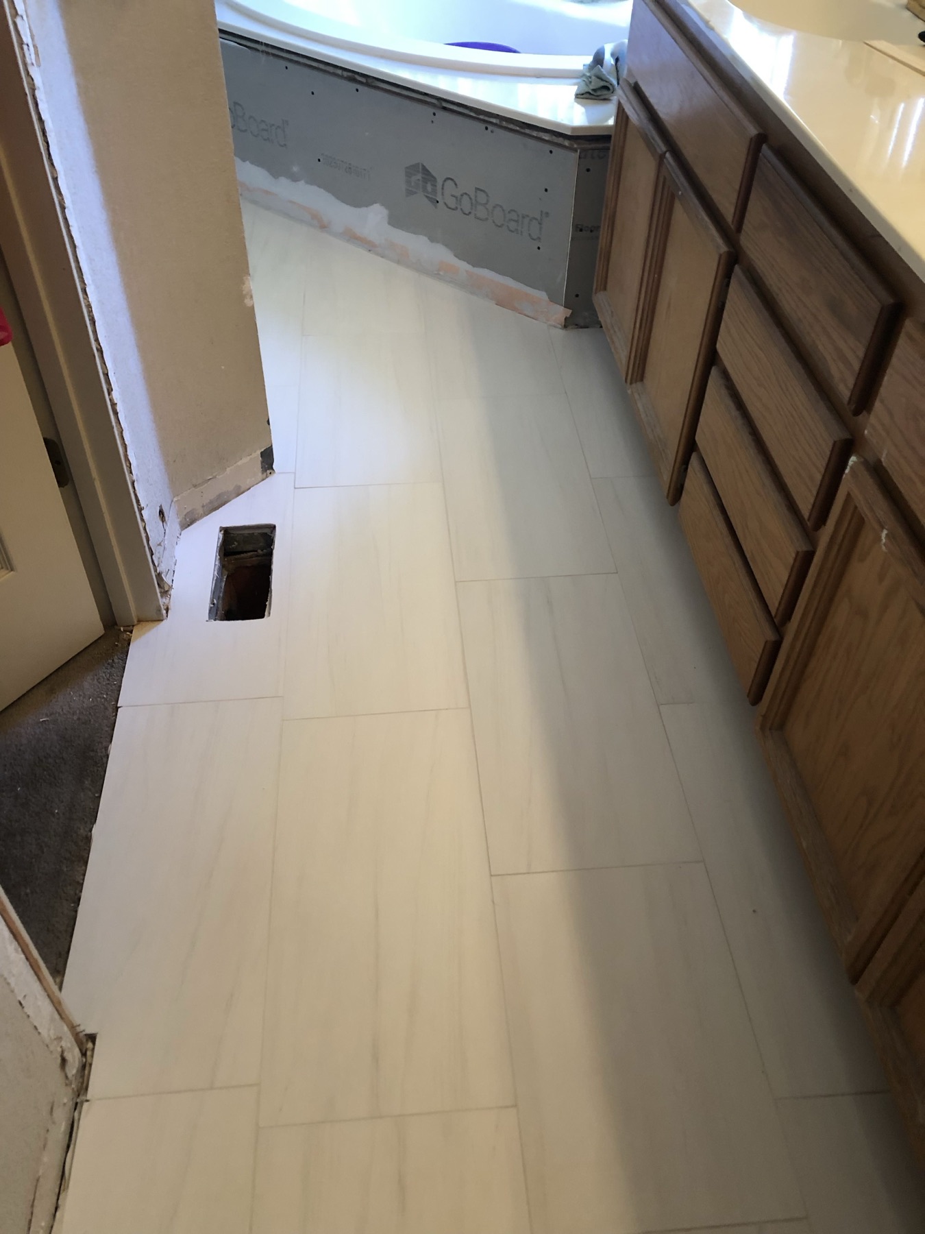 Finished bathroom floor in light plank tile running past wood vanity cabinets