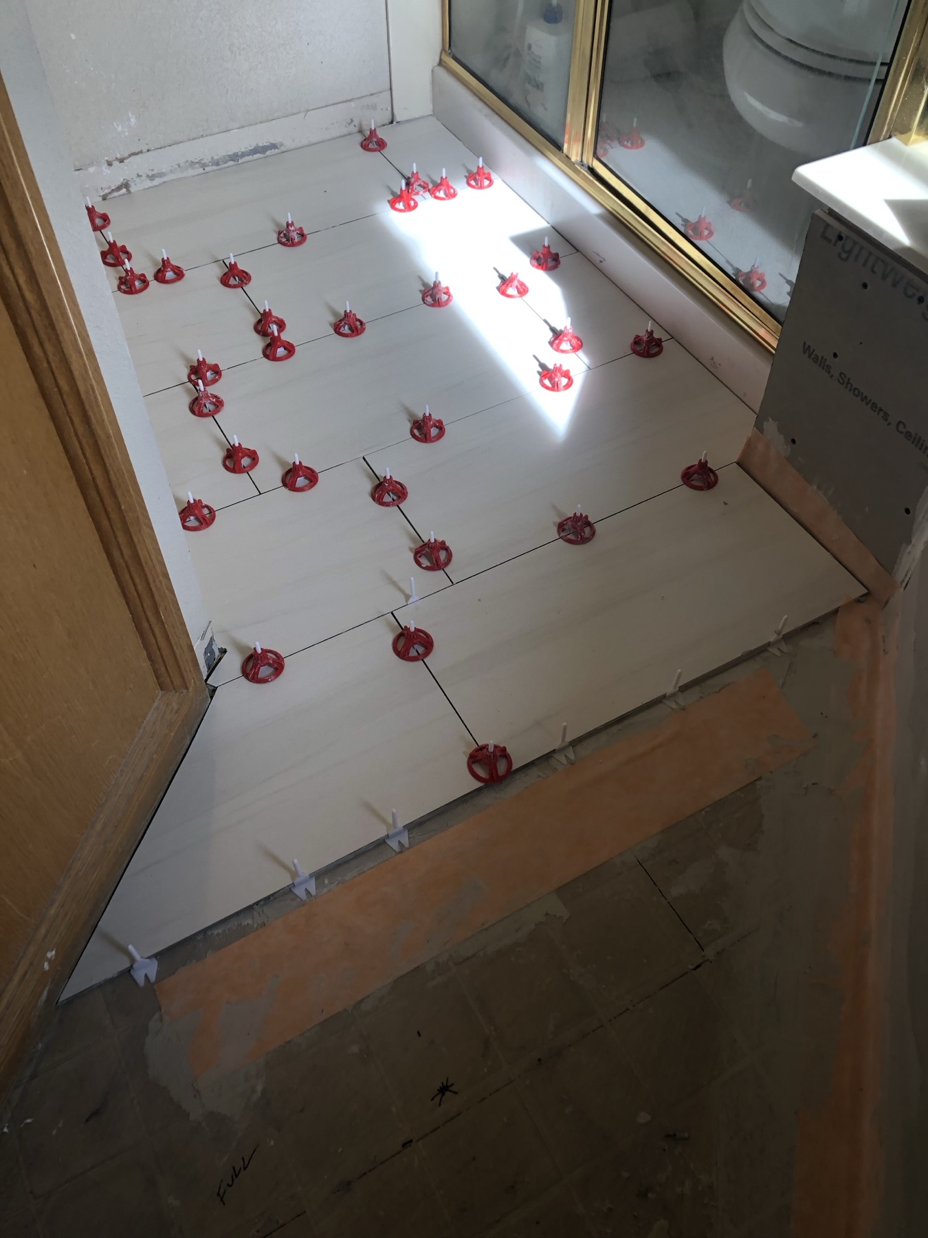 Light plank tile being set on a bathroom floor with red leveling clips