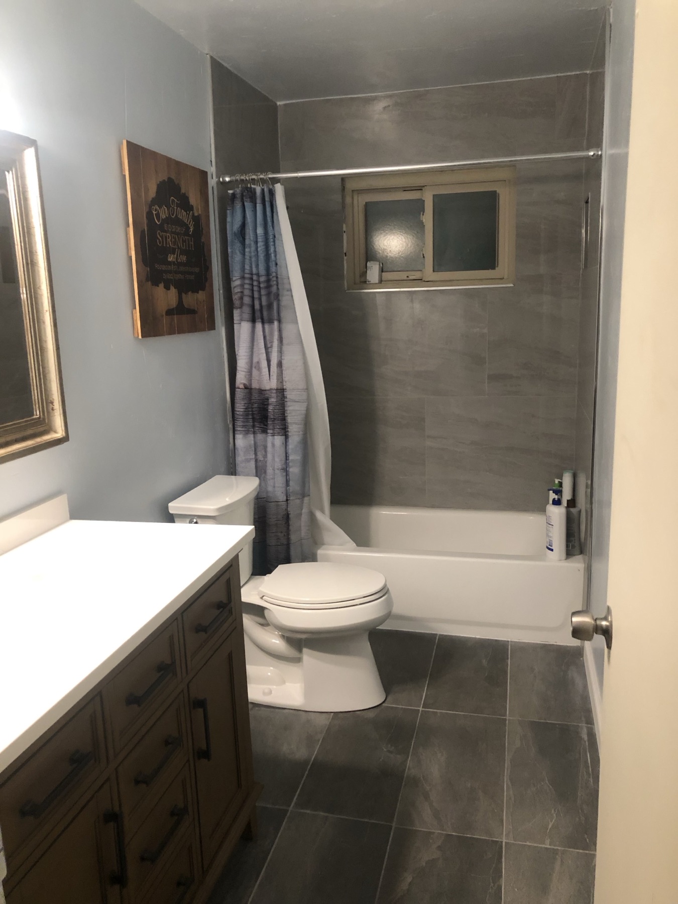 Finished bathroom with a gray tiled tub surround, vanity and dark tile floor