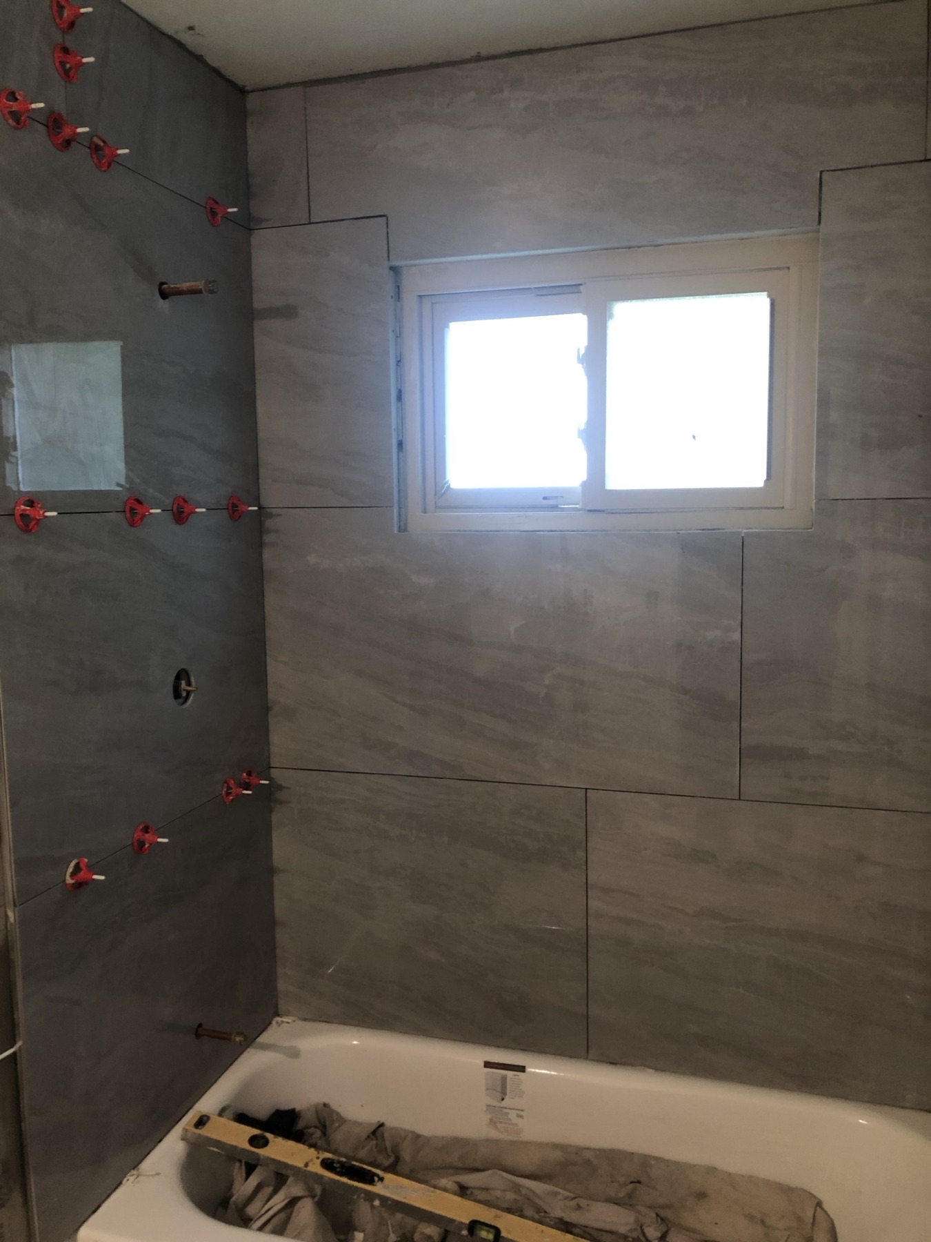Large gray wall tile being set around a bathtub with a leveling system