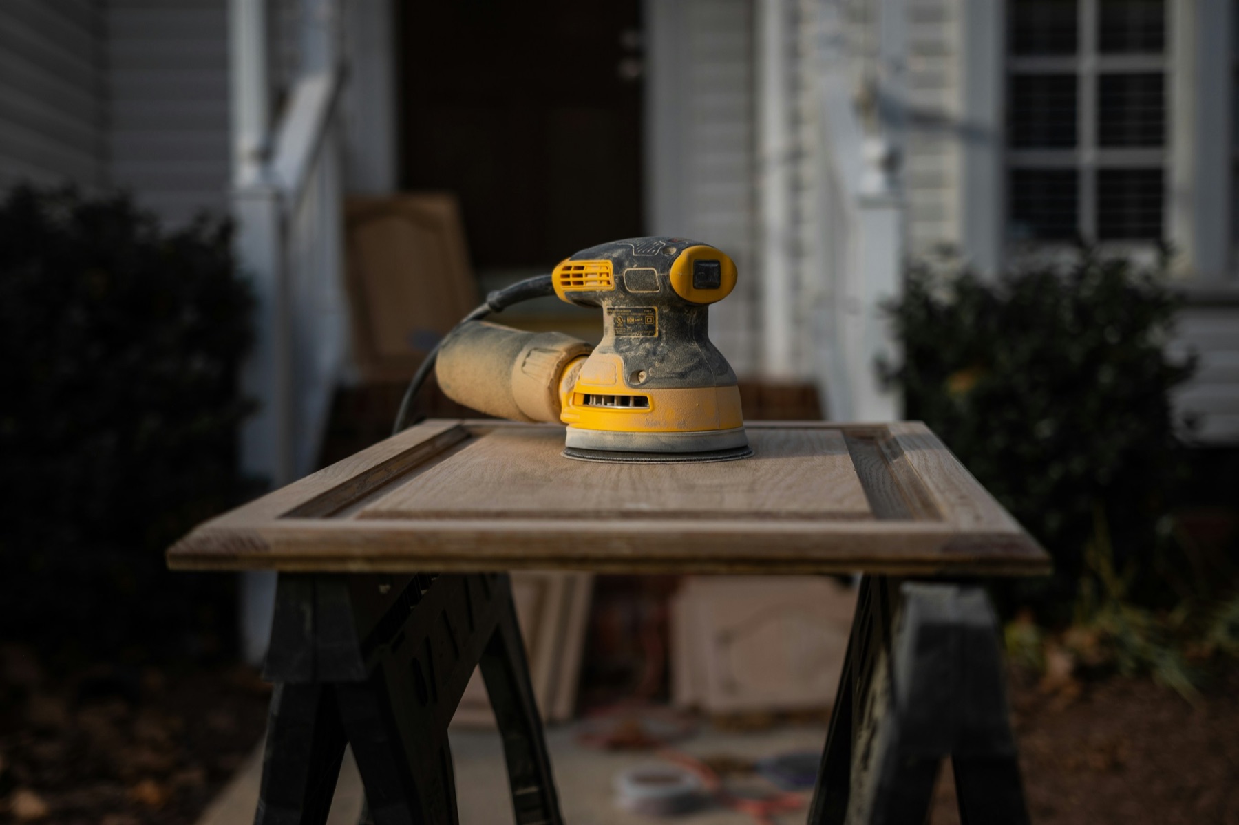 Orbital sander on a raised-panel cabinet door set on sawhorses, ready for refinishing