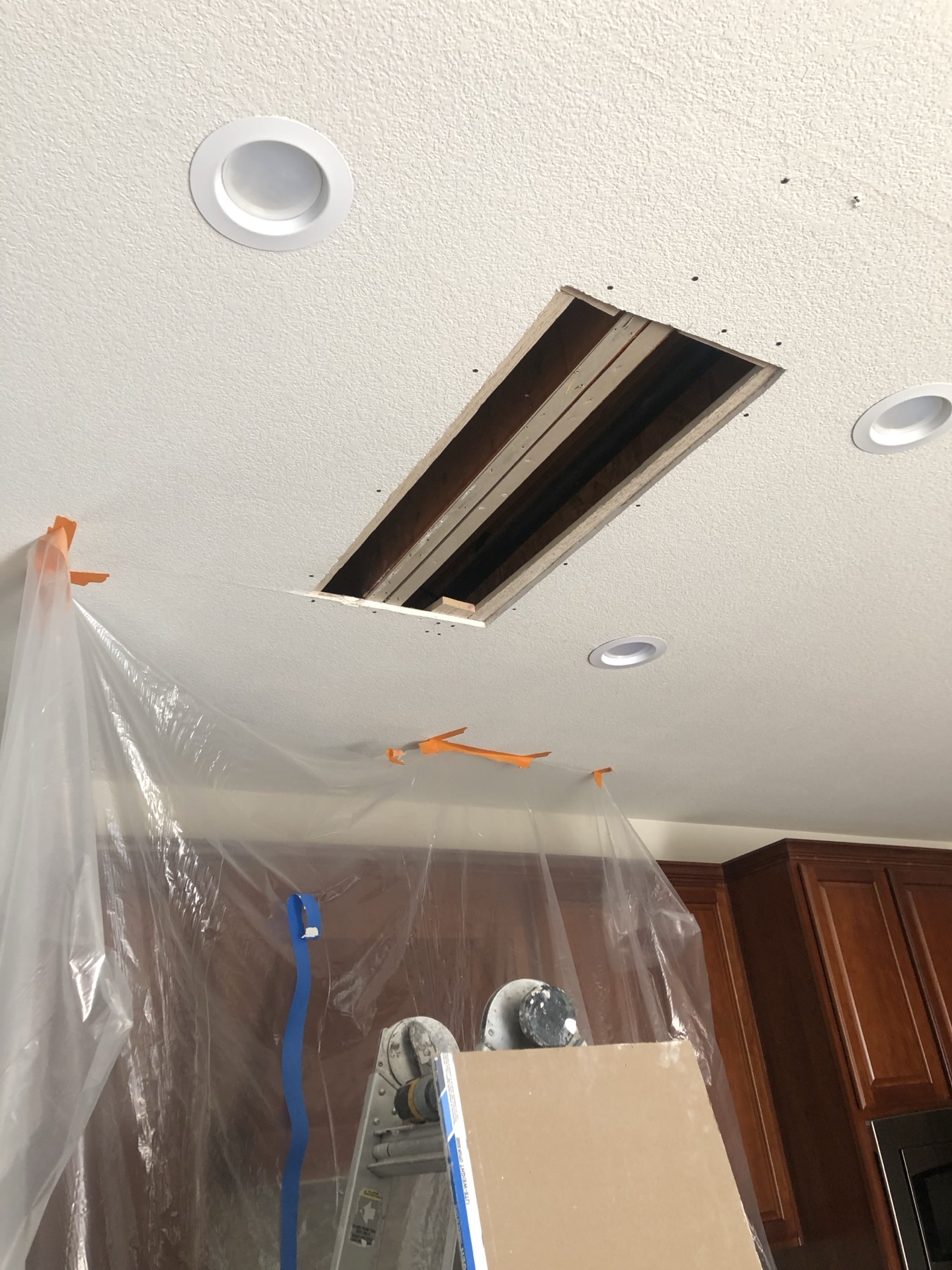 Ceiling opening above taped plastic sheeting and a ladder during drywall repair