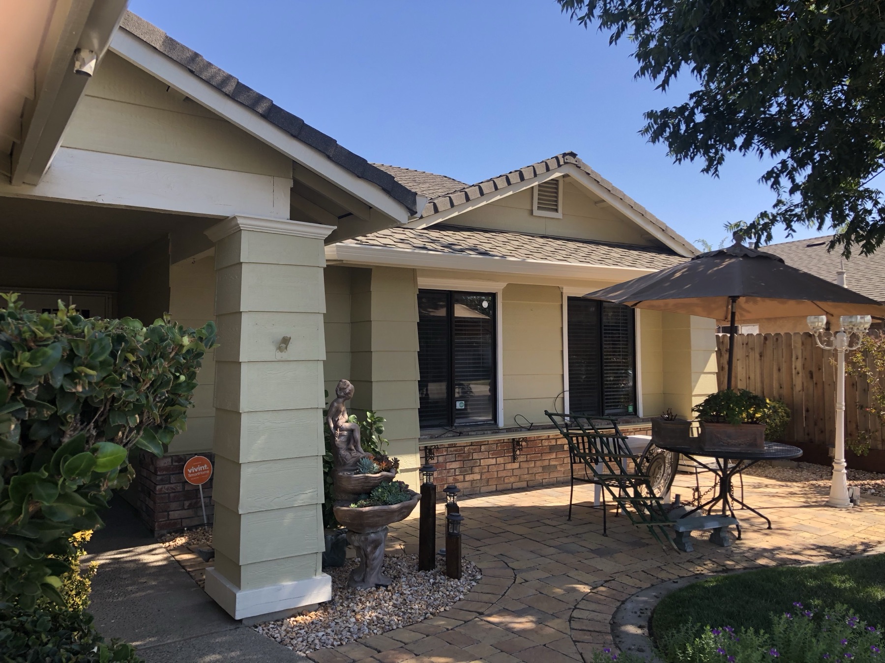Side of a sage green home with cream columns beside a covered brick patio