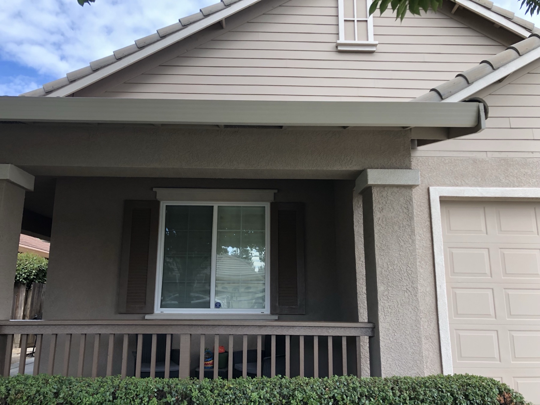 Freshly painted tan stucco home with a dark brown porch railing and trim