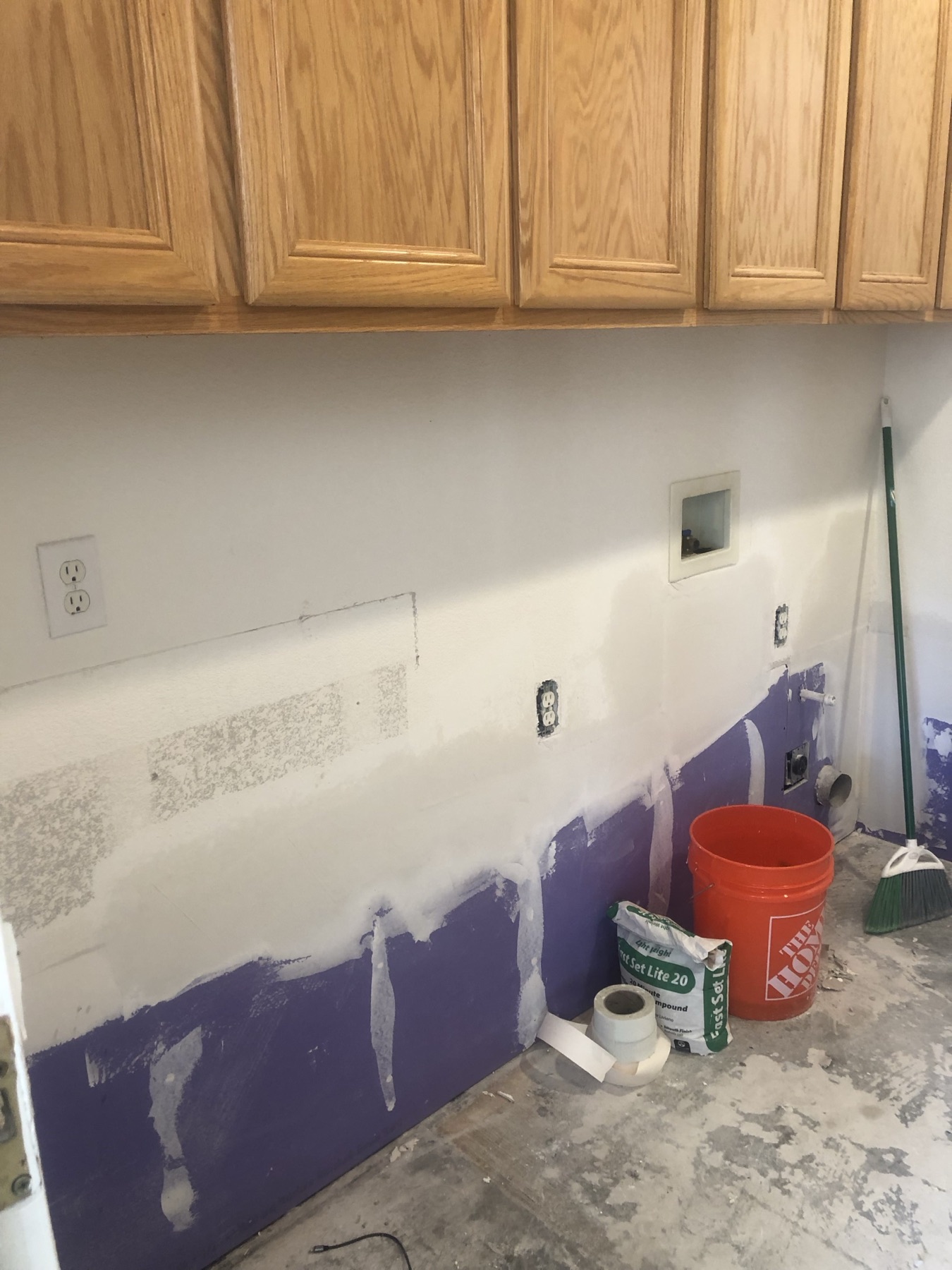 Laundry room wall mid-repair with fresh joint compound over new drywall