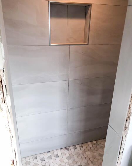 Renovated shower with large gray wall tile, a built-in niche and a pebble-stone floor